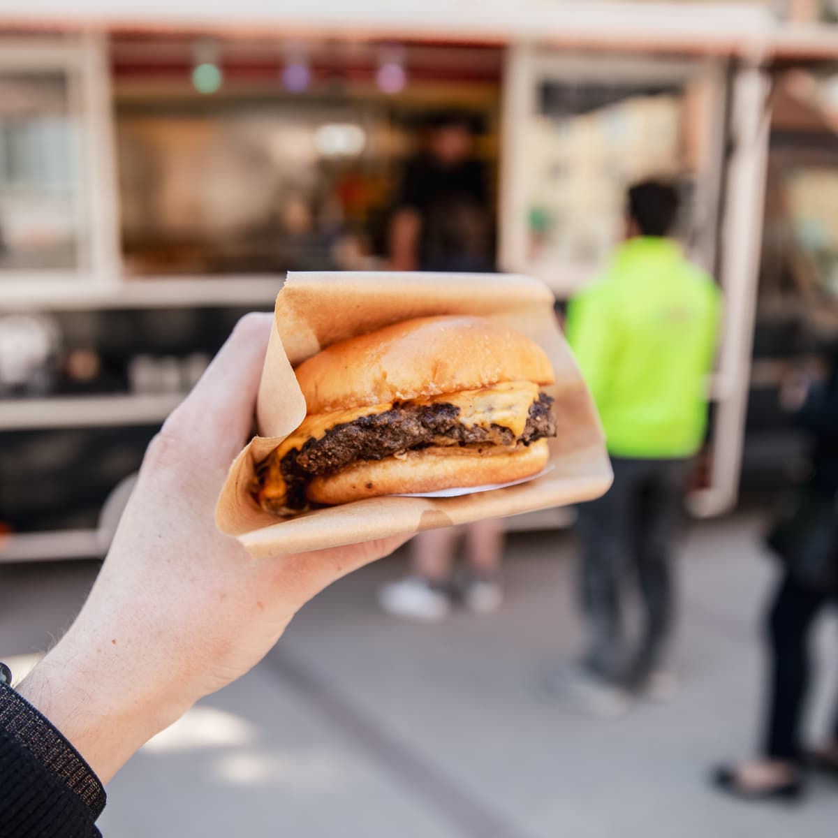 En person som håller en hamburgare framför en foodtruck.